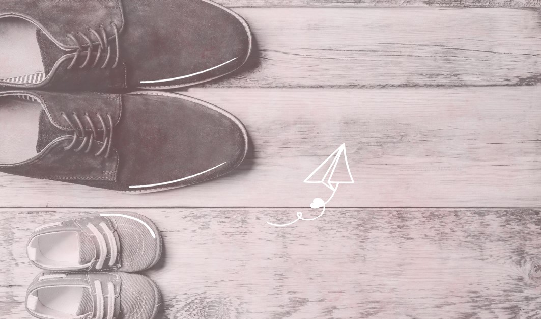 Adult and baby shoes on a rustic wooden background with a paper airplane illustration, symbolizing family planning and fertility. Image